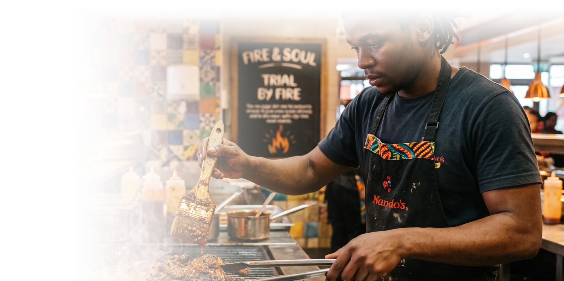 A griller turning chicken over the flames in a Nando's kitchen